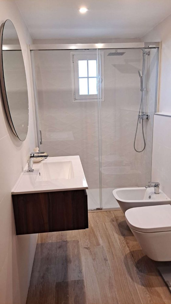 Baño reformado por Vita Reformas con plato de ducha, mampara y suelo imitación madera