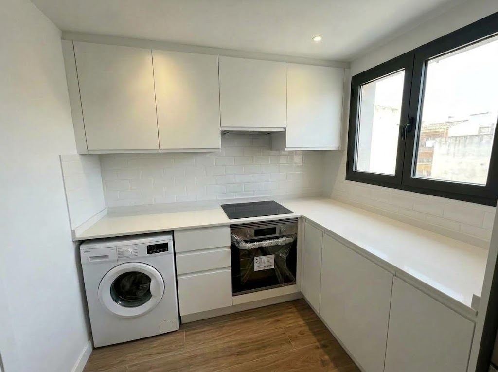 Cocina reformada en blanco con muebles lisos y encimera clara